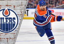 Edmonton Oilers defenseman Evan Bouchard looking focused on the ice, surrounded by action, representing NHL trade rumors.