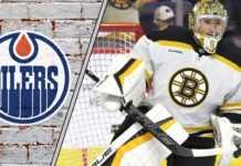 An image of Jeremy Swayman in his Boston Bruins gear, looking focused during a game, with the Edmonton Oilers logo faintly in the background, suggesting a potential trade.