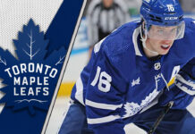 An intense, focused shot of Mitch Marner in his Toronto Maple Leafs jersey, looking up the ice during a game, with the crowd blurred in the background, highlighting the weight of his decision.