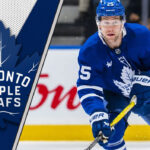 Toronto Maple Leafs defenseman Brandon Carlo skates with the puck during an NHL game, amidst recent NHL trade rumors connecting him to an offseason move