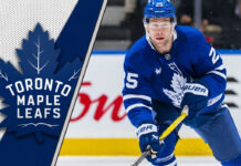 Toronto Maple Leafs defenseman Brandon Carlo skates with the puck during an NHL game, amidst recent NHL trade rumors connecting him to an offseason move