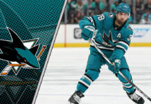 San Jose Sharks defenseman Mario Ferraro skates with the puck during an NHL game, with the San Jose Sharks logo on display