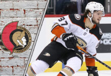 An action shot of Mason McTavish in his Anaheim Ducks jersey, skating with the puck during an NHL game, with the Ottawa Senators logo in the corner.