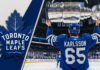 Erik Karlsson of the Toronto Maple Leafs, viewed from behind wearing his #65 jersey, hoists the Stanley Cup above his head at center ice in a packed Scotiabank Arena.
