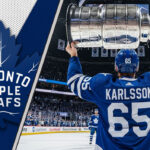 Erik Karlsson of the Toronto Maple Leafs, viewed from behind wearing his #65 jersey, hoists the Stanley Cup above his head at center ice in a packed Scotiabank Arena.