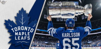 Erik Karlsson of the Toronto Maple Leafs, viewed from behind wearing his #65 jersey, hoists the Stanley Cup above his head at center ice in a packed Scotiabank Arena.