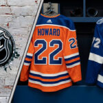 The backs of Isaac Howard's #22 Edmonton Oilers jersey and Sam O'Reilly's #72 Tampa Bay Lightning jersey hang side-by-side in an NHL locker room stall, symbolizing the recent trade.
