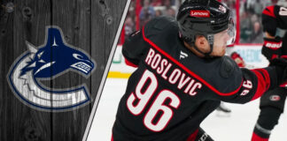 Jack Roslovic in his Carolina Hurricanes uniform, looking on during an NHL game. The background shows the ice and stands and the Canucks logo to the left