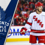 Are the Maple Leafs Targeting a High-Risk, High-Reward Winger to Bolster Their Offense? Free agent forward Jack Roslovic skates in his Carolina Hurricanes jersey, with the Toronto Maple Leafs logo in the background, representing trade rumors.