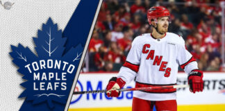 Free agent forward Jack Roslovic skates in his Carolina Hurricanes jersey, with the Toronto Maple Leafs logo in the background, representing trade rumors.