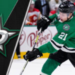 Dallas Stars forward Jason Robertson skates with the puck, with the backdrop of the arena lights, amidst ongoing contract negotiations.