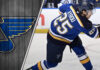 St. Louis Blues forward Jordan Kyrou takes a slapshot during an NHL game, with the Blues logo visible in the background.