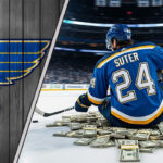 Pius Suter in St. Louis Blues jersey, sitting on money at center ice.