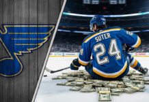Pius Suter in St. Louis Blues jersey, sitting on money at center ice.