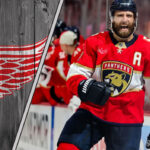 Aaron Eblad celebrating a goal in a Florida Panthers jersey with the Detroit Red Wings logo to the left