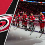 The Carolina Hurricanes team standing on the ice, preparing for a game, with the crowd cheering in the background.