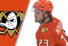 Anaheim Ducks center Mason McTavish skates with the puck during an NHL game, with Anaheim Ducks logo in the background
