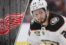 An image of Mason McTavish in his Anaheim Ducks jersey, looking focused during a game, with the Detroit Red Wings logo in the background.