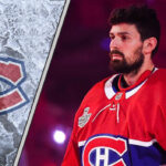 Montreal Canadiens goalie Carey Price looks on from the bench during an NHL game, with the Montreal Canadiens logo visible in the background.