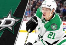 Dallas Stars forward Jason Robertson skates with the puck during an NHL game, with the Dallas Stars logo in the background.