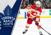 Former Calgary Flames forward Dillon Dube skating with the puck during an NHL game with the Toronto Maple Leafs logo to the left