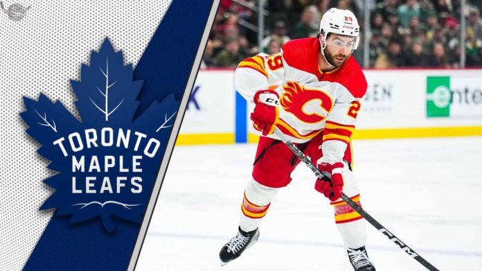 Former Calgary Flames forward Dillon Dube skating with the puck during an NHL game with the Toronto Maple Leafs logo to the left