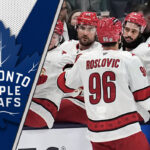 Jack Roslovic skates in his Carolina Hurricanes jersey, with the Toronto Maple Leafs logo superimposed in the corner representing trade interest.