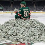 Kirill Kaprizov of the Minnesota Wild sits on a giant pile of money on the ice at his home arena.