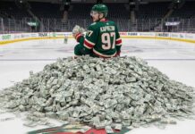 Kirill Kaprizov of the Minnesota Wild sits on a giant pile of money on the ice at his home arena.