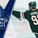 Minnesota Wild forward Kirill Kaprizov looks on thoughtfully during an NHL game, contemplating his future with the Toronto Maple Leafs logo to the left