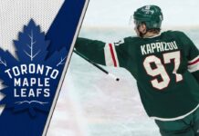 Minnesota Wild forward Kirill Kaprizov looks on thoughtfully during an NHL game, contemplating his future with the Toronto Maple Leafs logo to the left