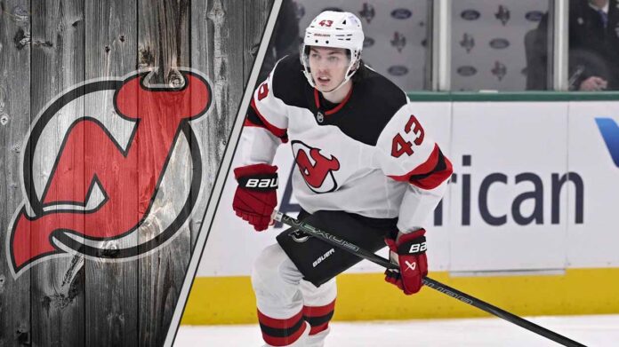 new-jersey-devils-luke-hughes-contract-dispute-2025 New Jersey Devils defenseman Luke Hughes skates with the puck during an NHL game, with the Devils logo in the background.