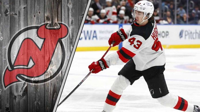 new-jersey-devils-luke-hughes-contract-negotiations New Jersey Devils defenseman Luke Hughes skates with the puck during an NHL game, with the Devils' logo visible in the background.
