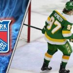 The New York Rangers’ Calculated Gamble for Kirill Kaprizov Image of Kirill Kaprizov skaking with the New York Rangers logo in the background.