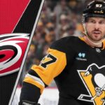 The Trade Destination for Sidney Crosby That No One Is Talking About Pittsburgh Penguins captain Sidney Crosby looks on thoughtfully during a game, with the Carolina Hurricanes logo faintly in the background.