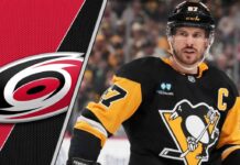 Pittsburgh Penguins captain Sidney Crosby looks on thoughtfully during a game, with the Carolina Hurricanes logo faintly in the background.