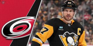 Pittsburgh Penguins captain Sidney Crosby looks on thoughtfully during a game, with the Carolina Hurricanes logo faintly in the background.