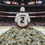 Hockey player in an Anaheim Ducks jersey with "LaCombe" and "2" on the back, wearing a helmet, sitting on a massive pile of money at center ice of the Anaheim Ducks home arena.