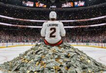 Hockey player in an Anaheim Ducks jersey with "LaCombe" and "2" on the back, wearing a helmet, sitting on a massive pile of money at center ice of the Anaheim Ducks home arena.