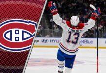 Montreal Canadiens forward Cole Caufield smiles and raises his stick, celebrating a goal on the ice.