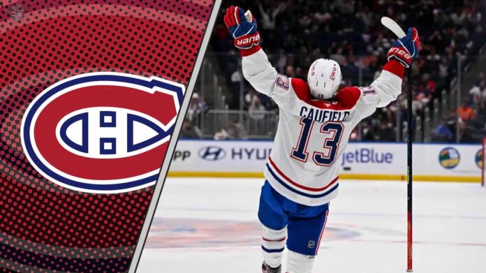 Montreal Canadiens forward Cole Caufield smiles and raises his stick, celebrating a goal on the ice.