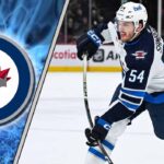 Winnipeg Jets Eyeing Defensive Help as Injury Exposes Blue Line Depth Close-up action shot of Winnipeg Jets defenseman Dylan Samberg skating with the puck during an NHL game.