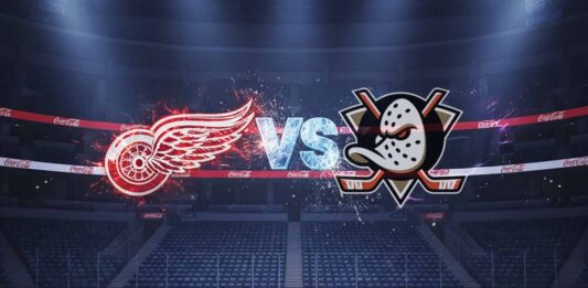 Detroit Red Wings and Anaheim Ducks logos facing off with ‘VS’ text at center on ice rink inside Ducks home arena under bright spotlights with Coca-Cola boards