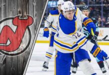 Buffalo Sabres forward Tage Thompson skates with the puck during an NHL game, with the New Jersey Devils logo in the background.