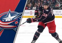 Columbus Blue Jackets forward Yegor Chinakhov skates with the puck during an NHL game, with the Blue Jackets logo visible in the background.