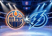 A wide-angle view inside a crowded hockey arena, featuring large, illuminated Edmonton Oilers and Tampa Bay Lightning logos colliding at center ice with a stylized metallic "VS" between them.