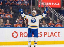 Why Alex Tuch Could Be the Savior the Edmonton Oilers Desperately Need Buffalo Sabres alternate captain Alex Tuch (#89), wearing a white away jersey, raises his arms in celebration while standing on the ice at Rogers Place. Behind him, the stands are filled with seated fans wearing Edmonton Oilers jerseys.