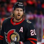 A close-up photograph captures Ottawa Senators forward Blake Coleman wearing his black home jersey, complete with the alternate captain's "A" and number 20, looking towards the camera with an open-mouthed expression during a game against the Calgary Flames.