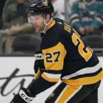 Pittsburgh Penguins defenseman Brett Kulak (27) wearing the team's black home jersey, skating on the ice and holding his hockey stick during a game.