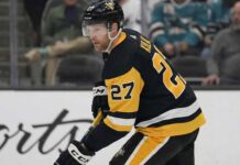 Pittsburgh Penguins defenseman Brett Kulak (27) wearing the team's black home jersey, skating on the ice and holding his hockey stick during a game.